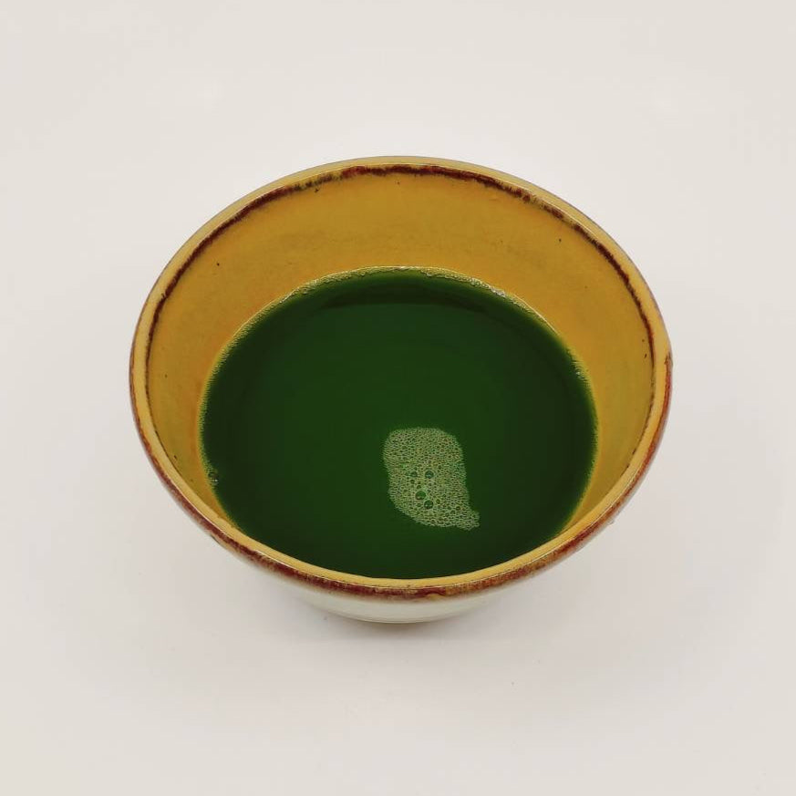 Ceramic cup with gold rim containing green liquid on a white background