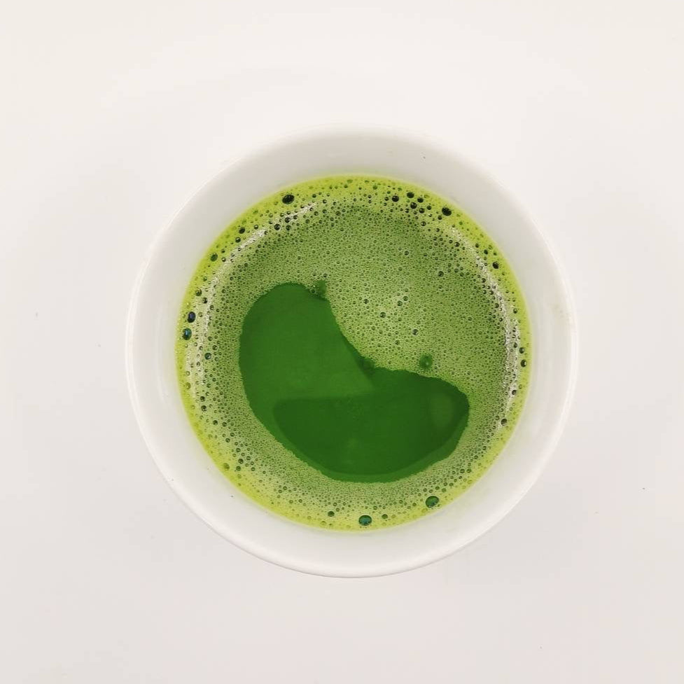 Green matcha tea in a white bowl on a light gray background