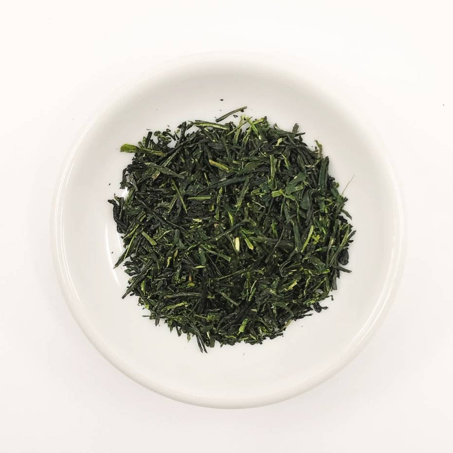 Green tea leaves in a white bowl on a white background