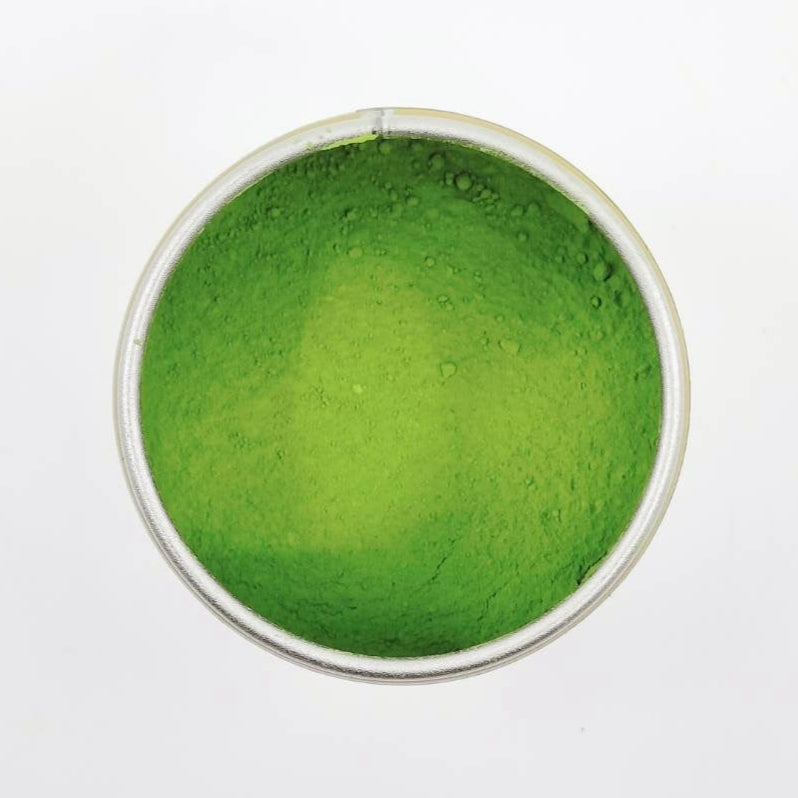 Green powder in a clear glass container on a white background