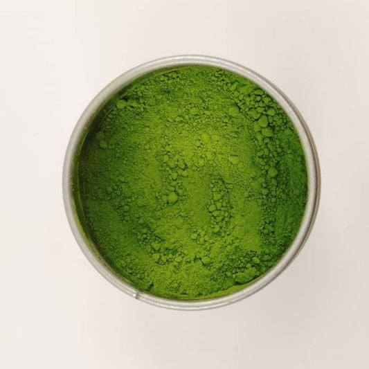 Green powder in a small metal container on a white background