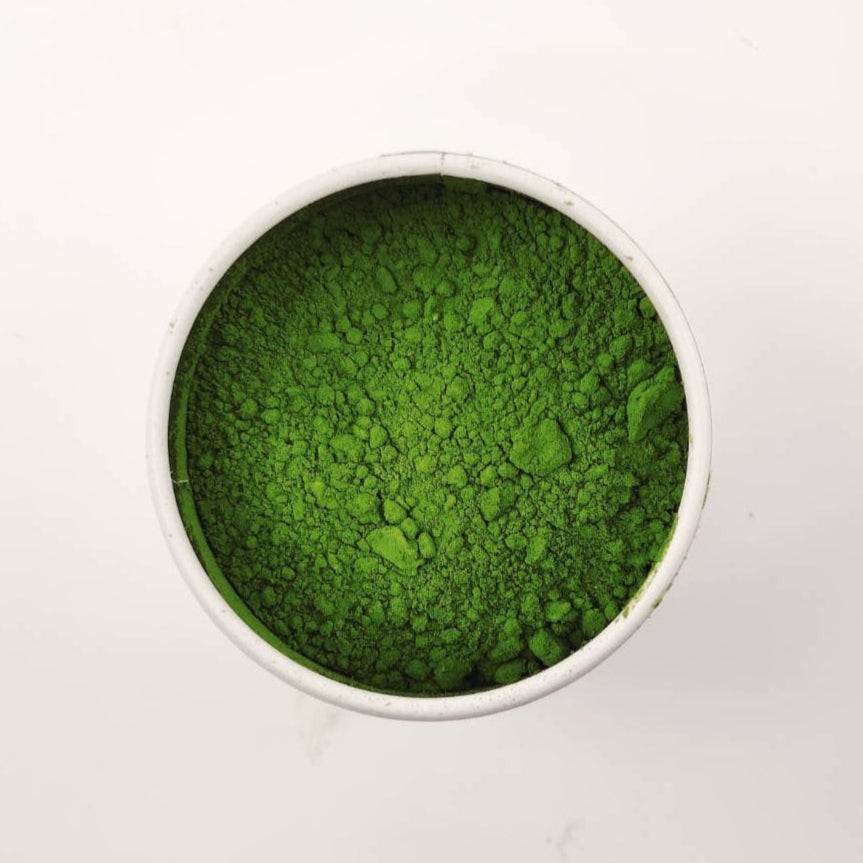 Green powder in a white container on a light gray background