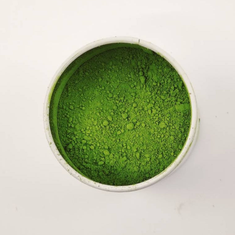 Green powder in a small white bowl on a light gray background