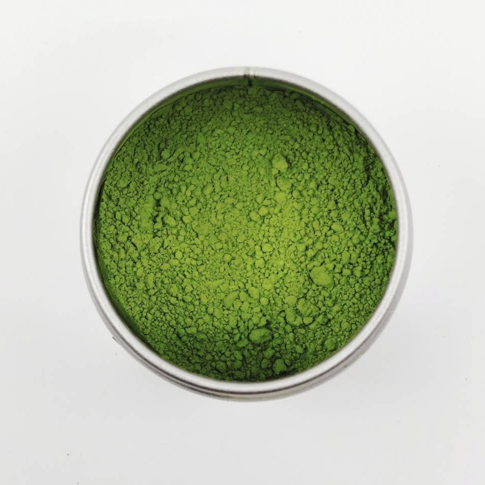 Green powder in a small metal container on a white background