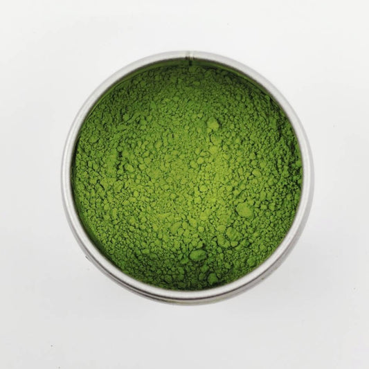 Green powder in a small metal container on a white background
