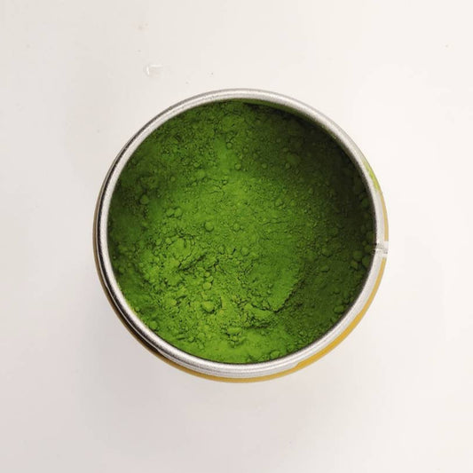 Green powder in a small metal container on a white background