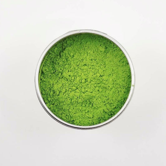 Green powder in a small metal container on a white background