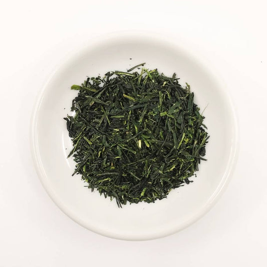 Green tea leaves in a white bowl on a white background